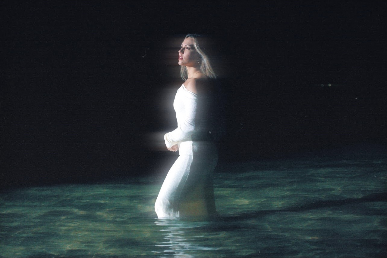 Madelynne West standing in water, illuminated against a dark background